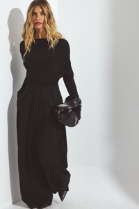 Zwarte lange mouwen top met gedrapeerd ontwerp, hoge taille zwarte wijde broek, en puntige zwarte schoenen; overal gladde texturen.