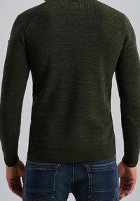 Maglione verde a maglia con un design testurizzato, dettagli a coste sulle spalle e orlo aderente, abbinato a jeans in denim blu.