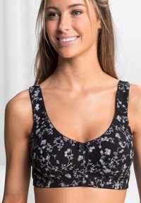 Reggiseno nero con motivo floreale bianco, tessuto morbido, spalline larghe, scollatura a barchetta e un piccolo dettaglio con fiocco al centro davanti.