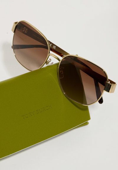 Okulary przeciwsłoneczne Tory Burch z brązowymi gradientowymi soczewkami, złotą metalową ramką i oprawkami w kolorze żółwim. Zielone etui z wytłoczonym logo marki.
