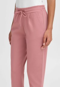 Light pink jogger pants with a soft, textured finish. Features a drawstring waistband and side pockets. Straight leg design.
