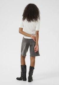 Haut blanc à manches courtes avec des pois noirs, associé à un short en denim gris et des bottes noires jusqu'aux genoux avec des boucles. Vue arrière.