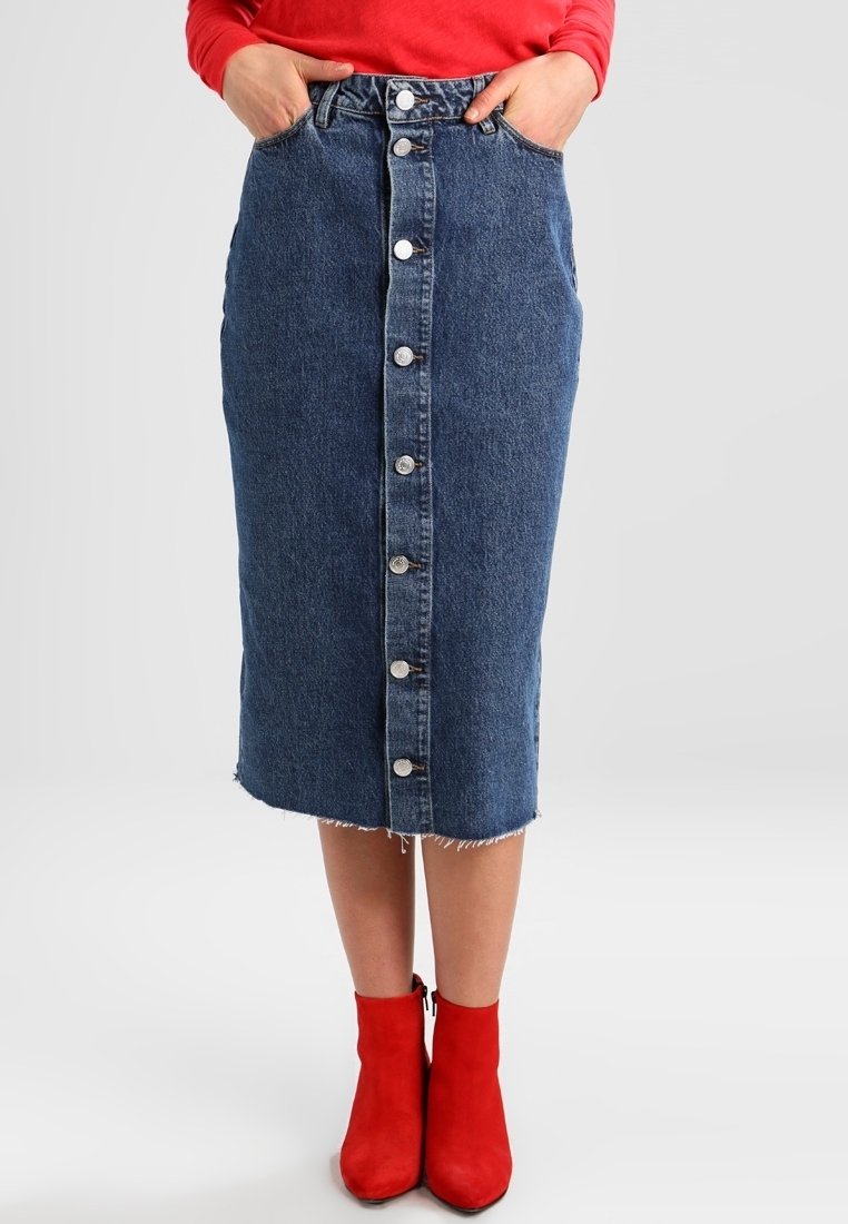 Tummansininen denimi-midi-hame, jossa on edessä napit, purjehtiva helma ja kaksi sivutaskua. Kontrastina hopeiset yksityiskohdat, yhdistettynä punaisiin nilkkabootseihin.