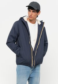 Navy puffer jacket with a zipper and hood, featuring a plush white lining and multi-colored accent stripes, designed for warmth and comfort.