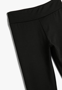 Sorte leggings lavet af glat, strækbart stof med en bred, flad talje. Designet er enkelt uden synlige mønstre eller hardware.