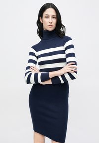 Πλεκτό φόρεμα με εφαρμοστή γραμμή, με navy μπλε και λευκές ρίγες, ψηλό γιακά και μακριά μανίκια με ριγέ λεπτομέρειες.