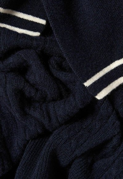 Jersey de punto azul marino con textura acanalada, con rayas blancas en el cuello. El material parece suave y ligeramente peludo.