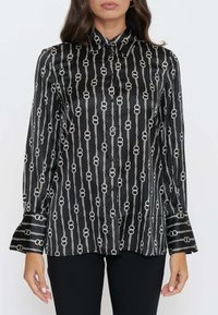 Blusa in satin nero con motivo a catena in argento. La camicia ha un colletto a punta e maniche a campana, con chiusure a bottone.