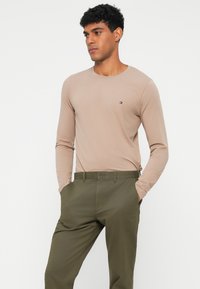 Beżowa koszula z długim rękawem, uszyta z miękkiego materiału, z małym logo na piersi, w połączeniu z oliwkowymi spodniami.