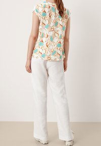 Haut à manches courtes avec un motif de feuilles colorées sur un fond crème ; associé à un pantalon large en lin blanc et des chaussures à plateforme.