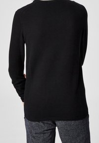 Haut noir à manches longues avec un motif en relief texturé, col rond et coupe décontractée, associé à un pantalon gris texturé.