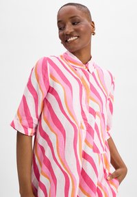Rosa und weißes Hemd mit gewellten Streifen in Rosa, Orange und Weiß. Verfügt über einen Kragen, einen Knopfverschluss und eine Brusttasche. Kurzarm.