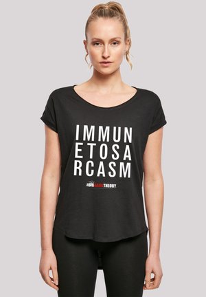 Svart T-skjorte med korte ermer laget av mykt stoff, med fet hvit tekst "IMMUN ETOS ARCASM" og "#BIGBANGTHEORY" i rødt. Rund halsutskjæring og avslappet passform.