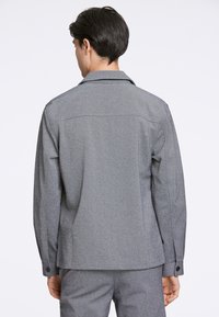Grau gewobenes Jacket mit Kragen, langen Ärmeln und Knopfmanschetten. Verfügt über ein schlichtes Rückendesign und subtile Textur.