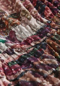 Gros plan sur un tissu plissé multicolore avec une broderie florale en relief dans des teintes de rose, vert, marron et rouge.