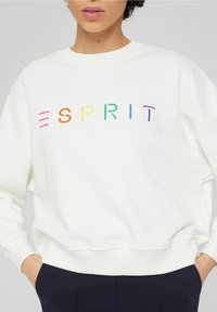 Sudadera blanca con letras bordadas multicolores que deletrean "ESPRIT". La tela tiene una textura suave y puños y dobladillo acanalados.