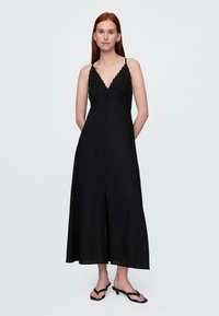 Schwarzes Maxikleid aus Leinen mit verstellbaren Spaghettiträgern, V-Ausschnitt und Schlitz vorne; verfügt über dekorative Ziernähte in der Mitte.