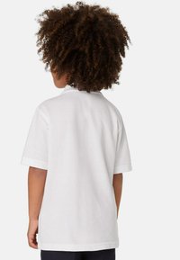 Polo shirt bianco a maniche corte, realizzato in cotone. Presenta un colletto classico e una vestibilità rilassata, con cuciture visibili e una consistenza liscia.