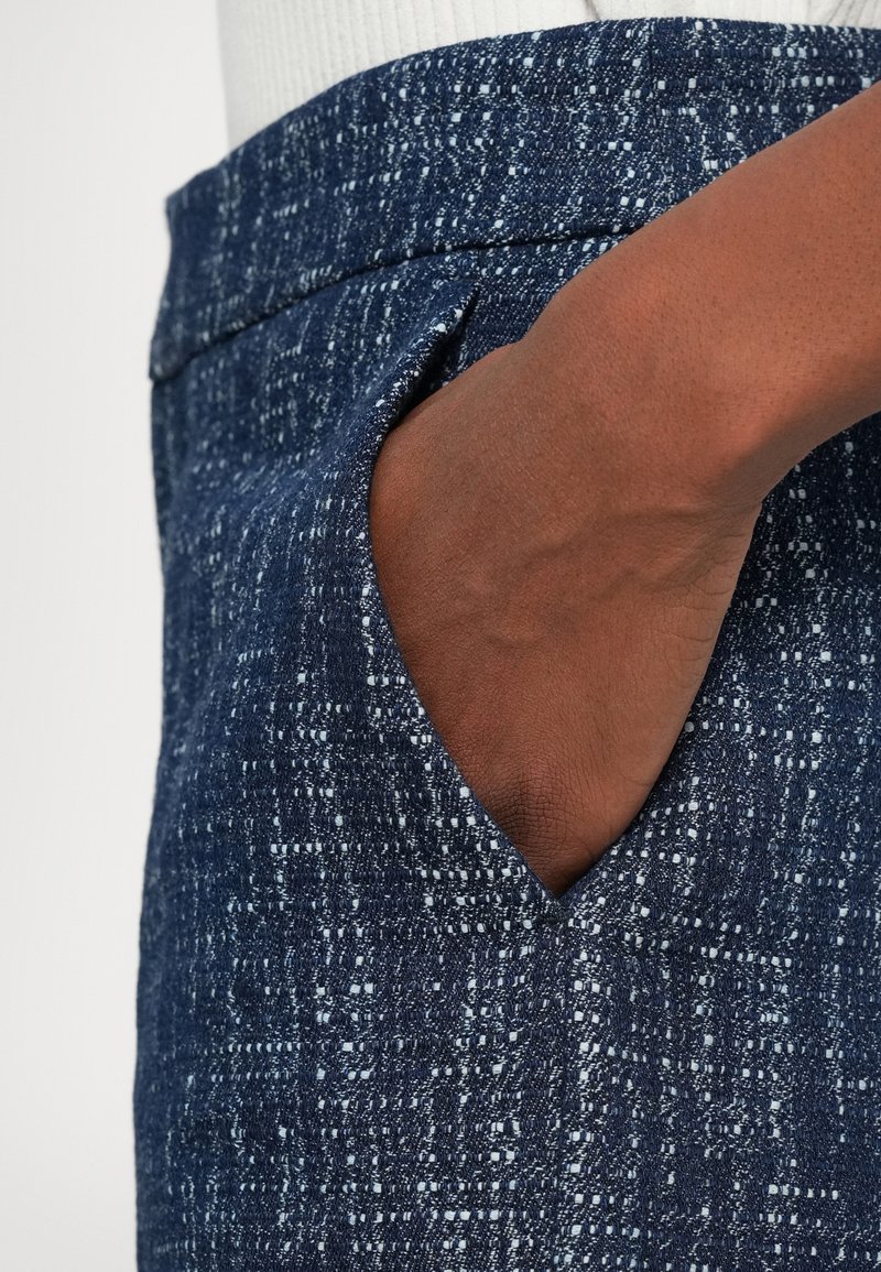 Dunkelblaue Jeansrock mit strukturiertem Muster. Verfügt über eine Taschen an der Seite und einen glatten Bund. Nahaufnahme des Stoffes und der Hand in der Tasche.