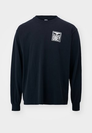 Schwarzes Langarm-Cotton-T-Shirt mit einem weißen quadratischen Grafikdruck, auf dem das Wort "OBEY" auf der linken Brustseite abgebildet ist. Rundhalsausschnitt und enganliegende Bündchen.
