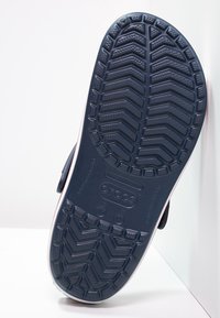 Semelle d'un sabot Crocs bleu marine montrant un motif de bande de roulement texturé et un logo en vue rapprochée et en angle.