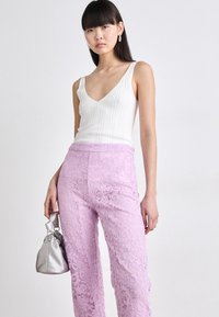 Witte geribbelde tanktop met een diepe V-hals, gecombineerd met lavendelkleurige kanten broek met een bloemenpatroon, en een kleine zilveren tas.