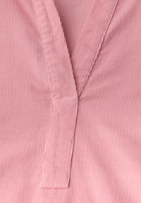 Rooze corduroy stof met een gestructureerde oppervlakte, voorzien van een afgeknipte kraag en zichtbare stiksels. De textuur is ribbelig en zacht.