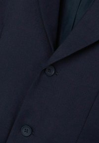 Blazer bleu foncé avec un tissu texturé, des revers fins et deux boutons noirs à l'avant pour la fermeture.