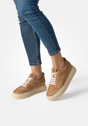 Beigefarbene Wildleder-Sneaker mit einer klobigen cremefarbenen Sohle, weißen Schnürsenkeln, abgerundeter Spitze und genähten Details an den Seiten.