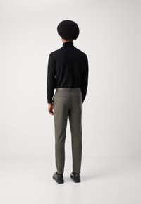 Tmavé dlouhé rukávy triko a olivově zelené kalhoty na míru, s hladkou texturou a slim fit. Černé kožené boty dotvářejí celkový vzhled.