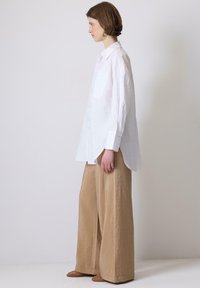 Camicia bianca oversize con colletto a punta, maniche lunghe e una tasca sul petto abbinata a pantaloni beige a gamba larga. Entrambi gli articoli sono in tessuto testurizzato.