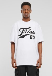 Hvit oversized T-skjorte med svart 'Fubu 05' grafikk. Myk bomullsstoff, korte ermer, rund hals og avslappet passform.