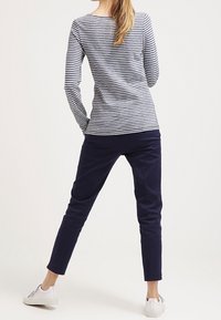 Maglietta a righe a maniche lunghe in blu navy e bianco abbinata a pantaloni blu navy. L'insieme presenta una vestibilità comoda ed è completato da sneakers bianche.
