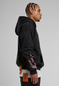 Sudadera negra de tejido suave con gráficos de llamas coloridas en las mangas, capucha ajustable y parches de logo en el dobladillo.