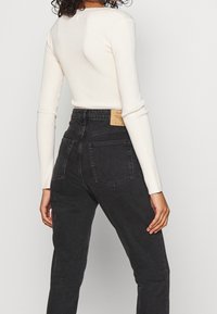 Hladký krémový top s dlouhým rukávem doplněný o vysoké černé džíny z denimu s koženou nášivkou, dvěma zadními kapsami a slim fit střih.
