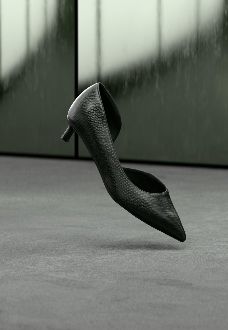 Μαύρο γυναικείο παπούτσι με ψηλό τακούνι και μυτερή μύτη, με υφή στην επιφάνεια και ανο ιχτή πίσω πλευρά. Το μικρό τακούνι αναδεικνύει το σχέδιο.