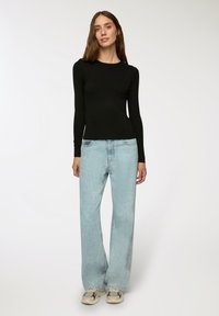 Czarny top z długim rękawem, dopasowany krój, zestawiony z jasnoniebieskimi szerokimi dżinsami. Sneakersy w kolorowy wzór blokowy. Gładkie tło.