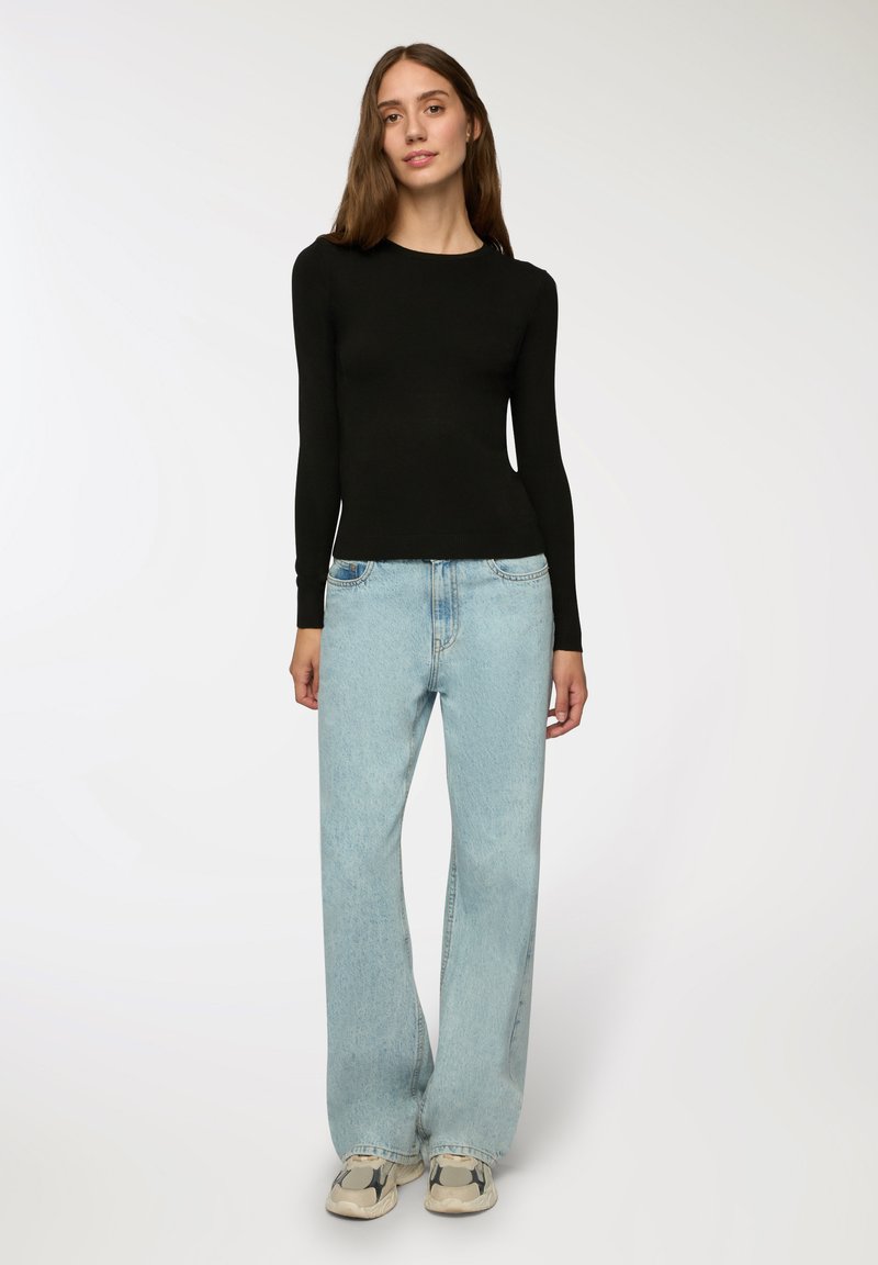 Czarny top z długim rękawem, dopasowany krój, zestawiony z jasnoniebieskimi szerokimi dżinsami. Sneakersy w kolorowy wzór blokowy. Gładkie tło.