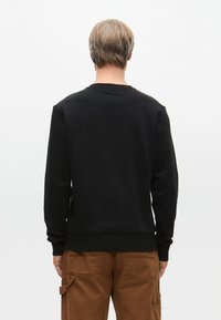 Fekete kapucnis pulóver bordázott mandzsettával és alsó szegéllyel, sima felülettel, kerek nyakkivágással, hátulról nézve, barna cargo nadrággal párosítva.