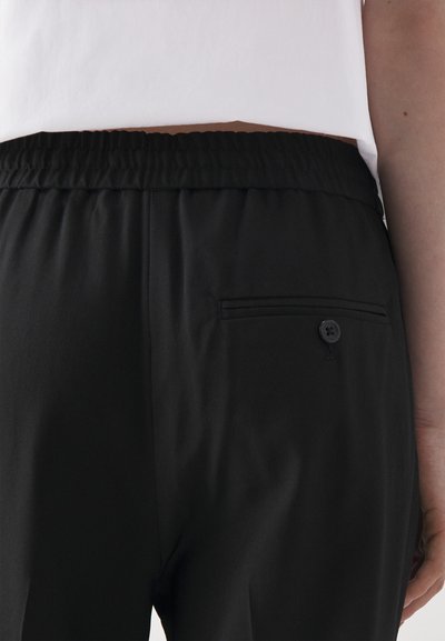 Black pants with an elastic waistband, featuring a small back pocket with a button detail; smooth texture and straight cut.