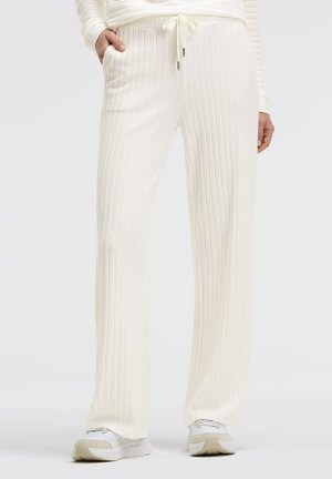 White ribbed lounge pants with a drawstring waist, side pockets, and a relaxed fit, paired with white sneakers.