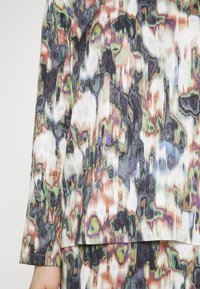 Ensemble haut à manches longues et jupe avec motif abstrait multicolore dans des tons verts, violets, noirs, blancs et bruns.
