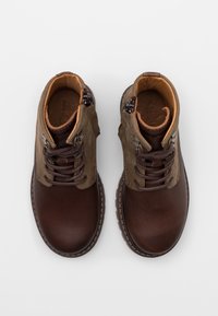 Bottines en cuir marron avec un bout arrondi, un laçage à l'avant et une fermeture éclair sur le côté, dotées d'une tige en tissu vert contrastant.