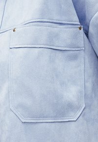 Φωτεινό γαλάζιο σουέτ τσέπη σακακιού με πτερύγιο ασφαλισμένο με δύο μεταλλικούς κοχλίες στις πάνω γωνίες.