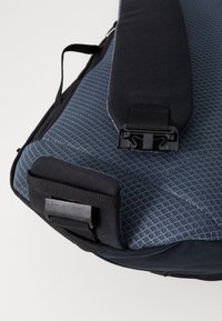 Blue textile bag with a textured surface, featuring a black strap and hardware clasp. The design includes a smooth, rounded base and adjustable features.
