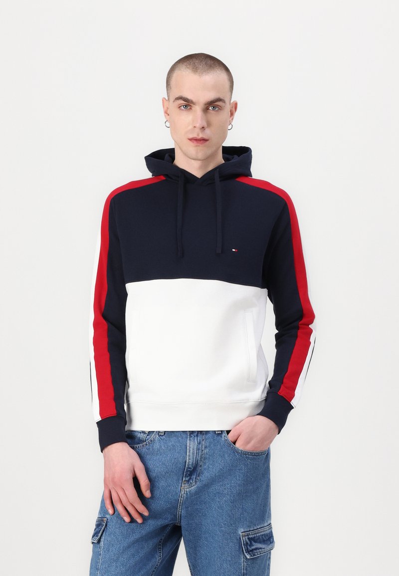 Navy, white, and red color-blocked hoodie with a kangaroo pocket, drawstring hood, and contrasting sleeve stripes. Smooth cotton fabric.