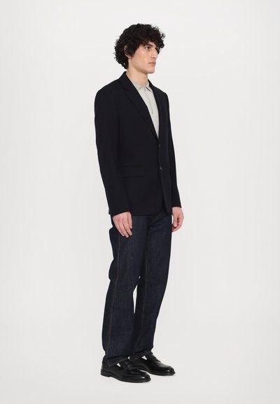 Merinovärinen blazer med notch-lapel, framfickor och knappar, kombinerat med ljusgrå polo, mörk denimjeans och svarta skor. Enkel, ren design.