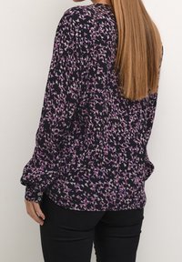 Langærmet bluse i mørk marineblå med et blomstermønster i lilla og lyserøde nuancer. Knaplukning ved manchetterne og en afslappet pasform med detaljer i ryggen.