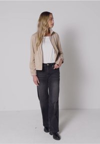 Béžová bomber bunda, bílý tričko s kulatým výstřihem, černé široké džíny. Hladká textura, lehký materiál, jednoduchý design. Černé boty.