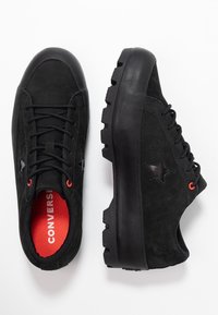 Czarne zamszowe trampki z wytrzymałą podeszwą, ozdobione czarną gwiazdą, pomarańczowymi przelotkami i czerwonym wkładem z napisem "CONVERSE".